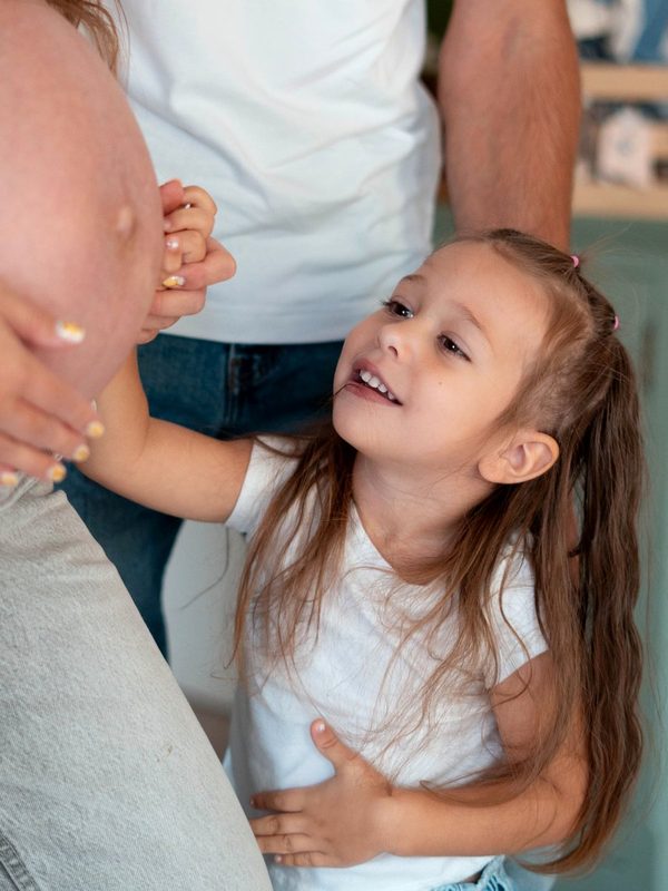 Little girl reaching up to her mother&rsquo;s baby bump